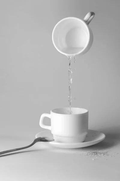 Water pouring from a white cup into another cup standing on the table
