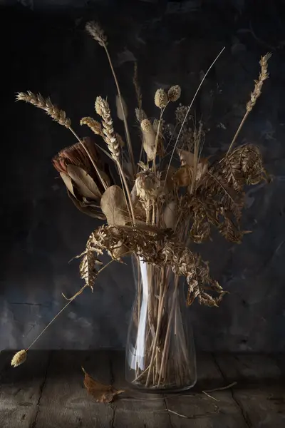 Glass vase with dried flowers and ears of corn against a gray wall