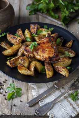 Kızarmış tavuk eti, ahşap bir masada siyah bir tabakta patates.