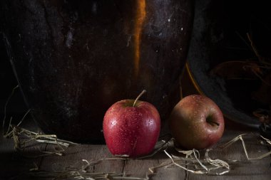 Büyük bir cam şişenin yanındaki tahta masada kırmızı elmalar.
