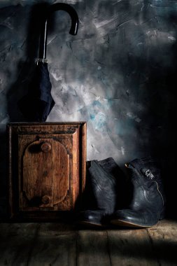Gri duvarın yanındaki komodinin yanında siyah deri ayakkabı ve şemsiye.