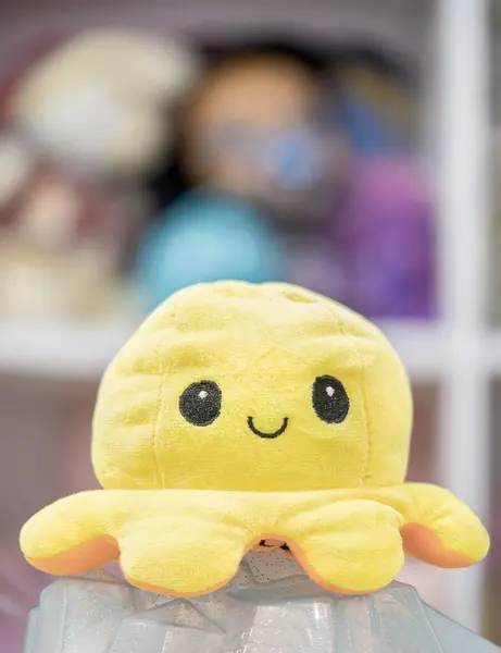 Ön planda sarı pelüş ahtapot, ahtapot şeklinde sarı pelüş bir oyuncak. Gülümseyen yüzü biraz kapris katıyor..