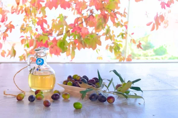 Olives on wooden table in the garden, olive oil in glass jug and autumn leaves background