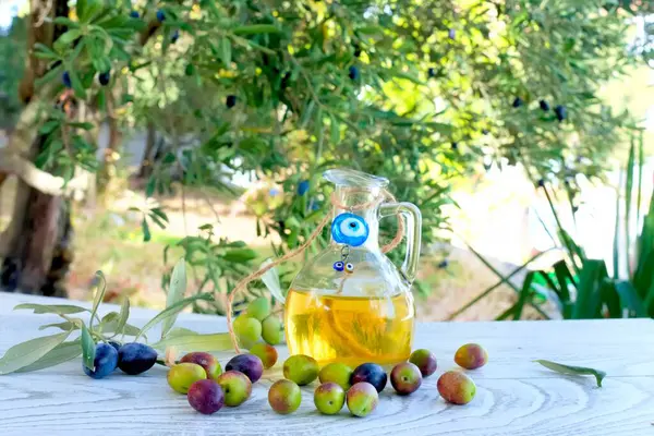 Olives on wooden table in the garden, olive oil in glass jug and olive tree background