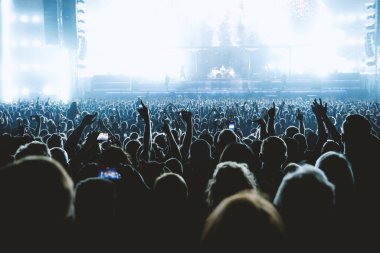 Bir müzik konseri sırasında kollarını kaldırmış bir grup insan ve inanılmaz bir ışık gösterisi. Siyah siluetler.