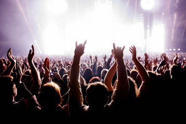 Bir müzik konseri sırasında kollarını kaldırmış bir grup insan ve inanılmaz bir ışık gösterisi. Siyah siluetler.