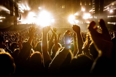 Bir müzik konseri sırasında kollarını kaldırmış bir grup insan ve inanılmaz bir ışık gösterisi. Siyah siluetler.