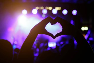 A person is making a heart sign during a concert of a favorite music band. Black silhouette
