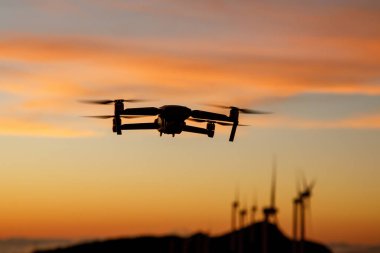 Flying drone in a sunset sky over wind turbine propeller farm. Green energy exploring
