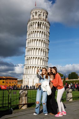 Pisa, İtalya - 27 Mart 2023: Üç mutlu kız, arkadaşlar ünlü eğik kule arka planında selfie çekiyorlar.