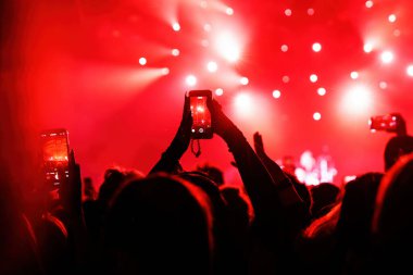 Konserde insanlar cep telefonlarıyla video veya fotoğraf çekiyorlar.