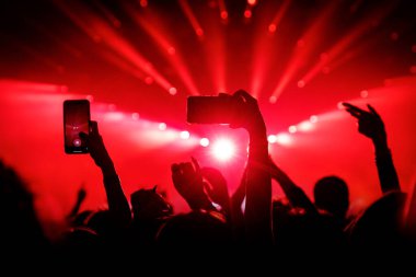 Konserde insanlar cep telefonlarıyla video veya fotoğraf çekiyorlar.