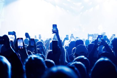 Konserde insanlar cep telefonlarıyla video veya fotoğraf çekiyorlar.