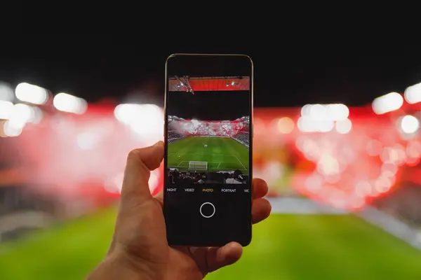 Fan hand with smartphone photographing football match. Using mobile phone camera at the stadium