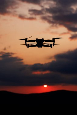 Gün batımında dağların üzerinden uçan bir dronun silueti.