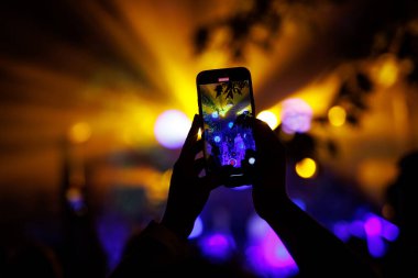 Bir müzik konserinde akıllı telefonlu bir el silueti.