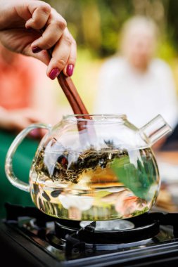 Çaydanlık demlenirken çaydanlığın yapraklarını karıştırır.