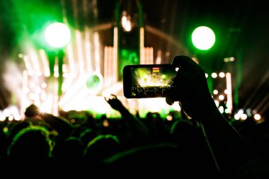 Cep telefonu kameralı bir elin silüeti ve konserin tadını çıkarmak..