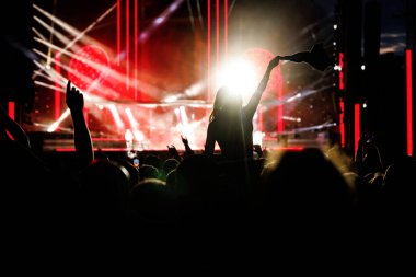 Müzik festivalinde konser veren kollarını kaldırmış mutlu bir kadına karşı sahne ışıkları..