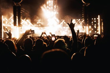 Performance of a popular group. The crowd with raised hands against the stage light.