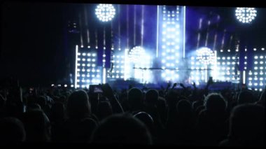 Bir müzik konseri ve ışık gösterisi sırasında el kaldıran kalabalığın siluetleri..