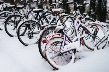 Kar kaplı bisikletler bir bisiklet parkında park edilmiş. Bisikletler eski moda, önünde büyük çamurluklar ve bir sepet var..