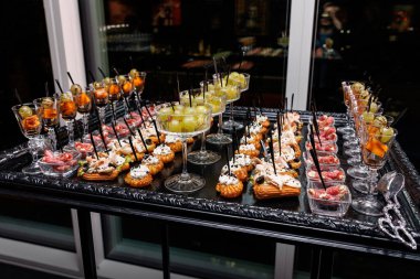 Şarap bardaklarıyla servis edilen karides, somon, peynir, kraker ve meyve gibi siyah ve gümüş tabakta çeşitli lezzetli ve tatlı atıştırmalıklar..