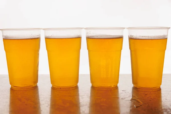 Plastic Disposable glasses of beer on a wooden surface and white background. The glasses are filled with golden beer and have a white foam on top.