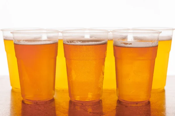 Plastic Disposable glasses of beer on a wooden surface and white background. The glasses are filled with golden beer and have a white foam on top.