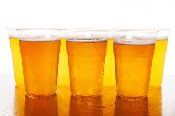 Four plastic glasses of frothy beer on a wooden table with a white backdrop.