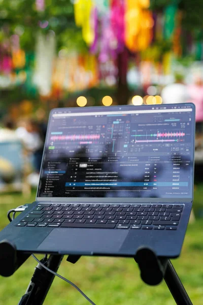 A festive scene of a laptop on a tripod with music software and vibrant decorations in the background.