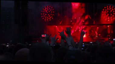Konserde kırmızı sahne ışıkları ve elleri havada bir grup insan..