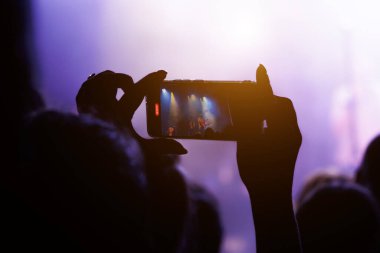 Kalabalık, sahne ışıkları ve akıllı telefonlu popüler bir müzik konserinin keyfini çıkarıyor..