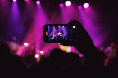 Sahne ışıklarıyla aydınlatılmış bir konserde dinleyiciler..