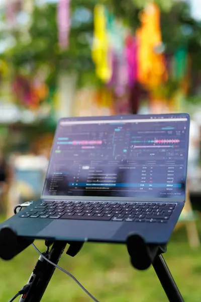 A DJ laptop with music editing software in a colorful outdoor festival.