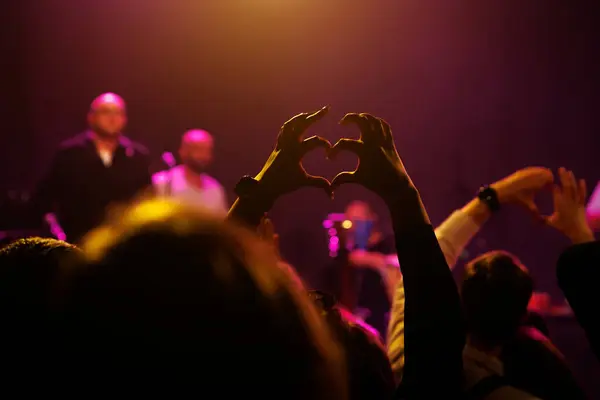A crowd of people at a concert making heart shapes with their hands