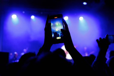 Canlı konserdeki kalabalığın siluetleri, kollar havada, selfie çekiyorlar.
