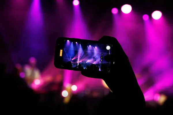 A concert-goer captures the live performance of a band on their phone.