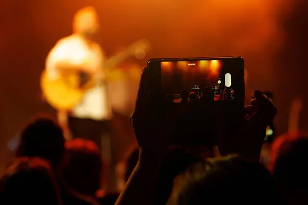 Group enjoying live music performance, photographing selfie on smartphone.