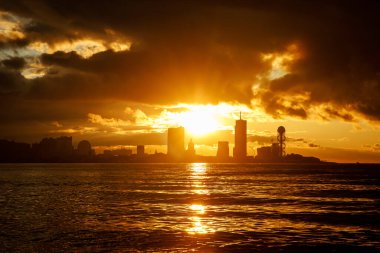 Güneşin binaların arkasında battığı ve suyun üzerine sıcak bir parıltı saçtığı güzel bir altın saat şehri..