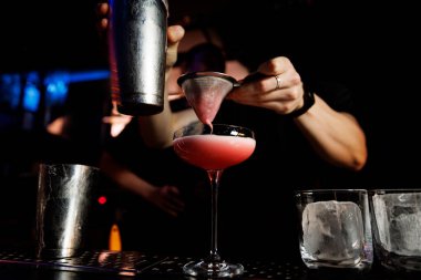 Barmen buzlu bardağa karışık bir kokteyl koyar.