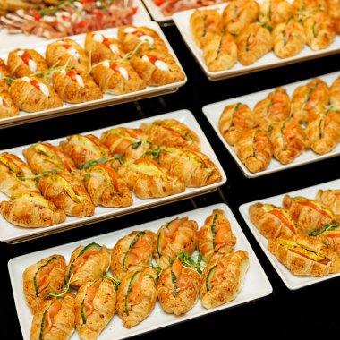 Taze otlarla süslenmiş altın kruvasanlar ve çeşitli lezzetli dolgular içeren bol bol gurme aperatifler.