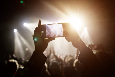 Canlı bir müzik olayının heyecan verici atmosferini yakalamak, izleyicilerden birinin akıllı telefonuyla fotoğraf çekmesi veya kaydetmesi..