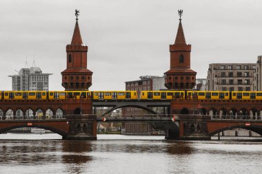 Sarı Berlin metro araçları kırmızı tuğla tarihi köprü boyunca ilerliyor. Kuleler arasında vagonlar