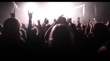 Performance of a popular group. The crowd with raised hands against the stage light.