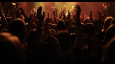 Silhouettes of people with raised hands against the stage light. Cheering crowd on the music show