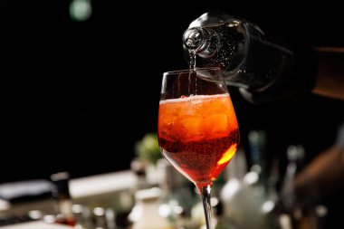 Aperol Spritz kokteyli yapan barmen bardağa buzla su döker.