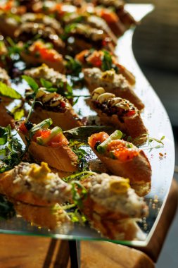 Somon, peynir ve otlar gibi taze malzemelerle kaplanmış canlı bir gurme bruschetta dizisi, cam tepside yenebilir çiçeklerle güzelce süslenmiş.