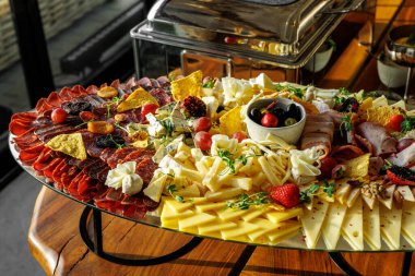 Tahta tepside çeşitli peynirler, sosisler ve diğer atıştırmalıklar dilimleniyor.