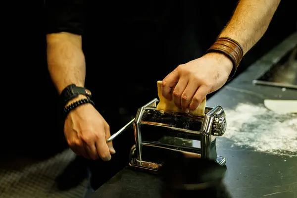 stock image Close-up of hands using a traditional pasta maker to flatten dough on a kitchen counter.